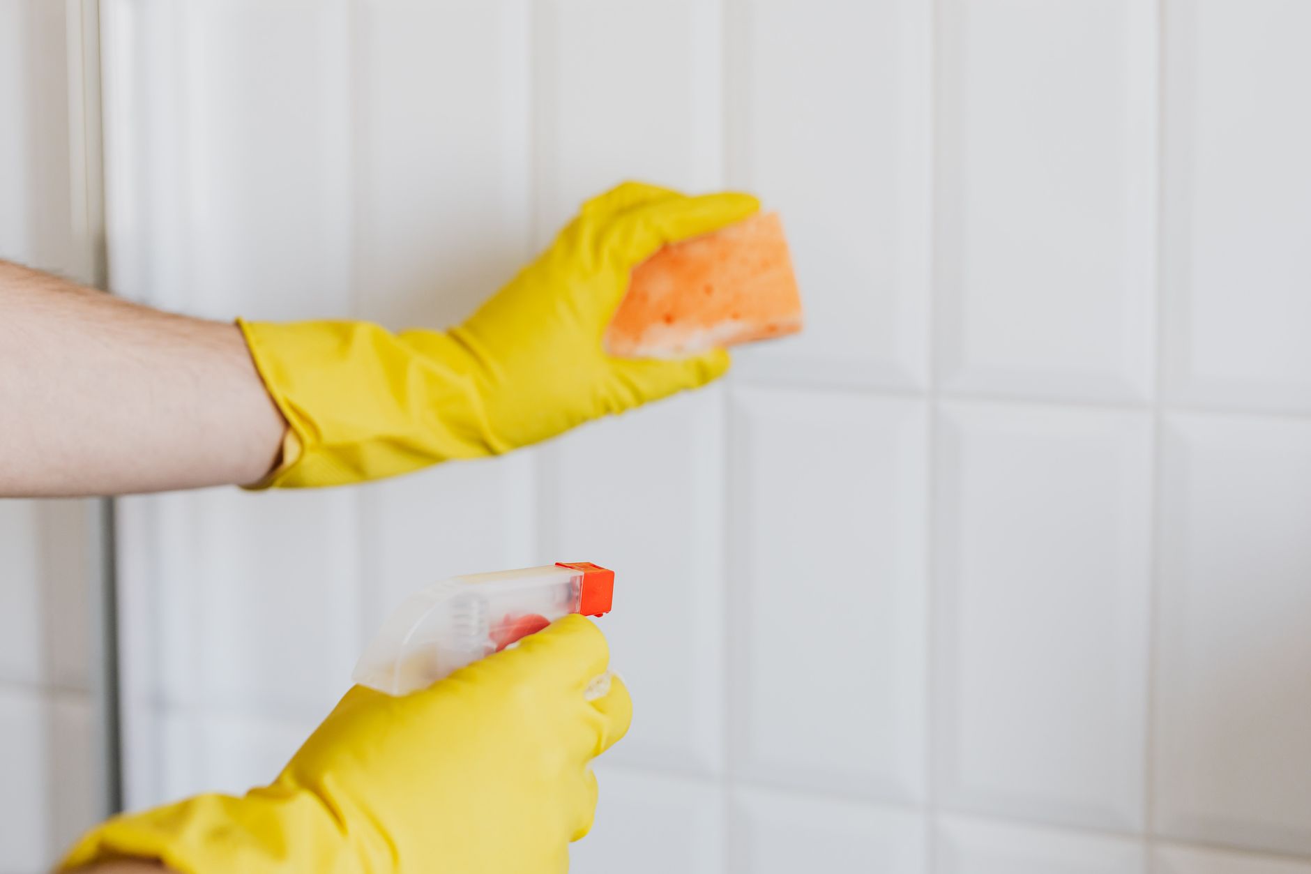 Gloved hand scrubbing bathroom tiles with a brush